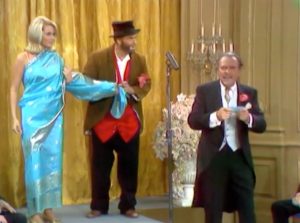 Freddie at the fashion show, unravelling the model in the saran, as Horace (Terry-Thomas) watches