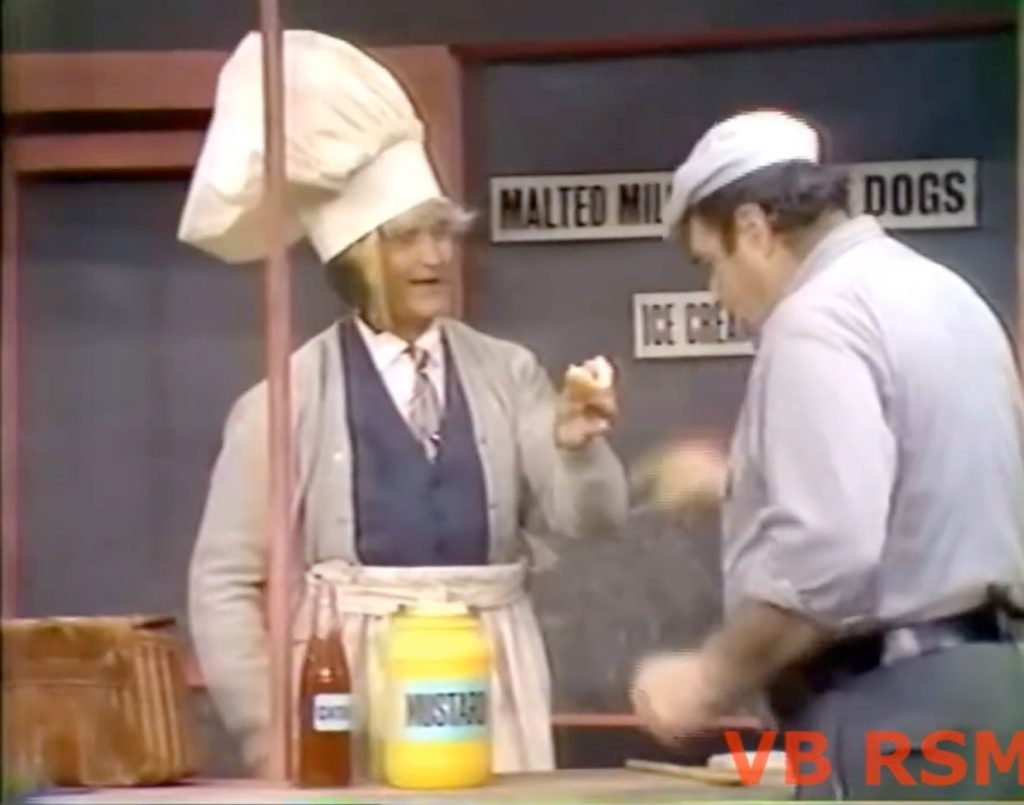 Pops selling a hot dog with LOTS of mustard! Note the fish in his hat …